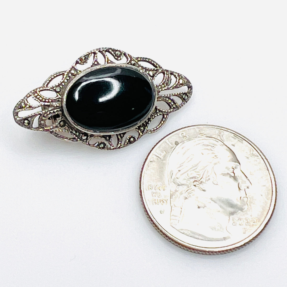 Petite black onyx and sterling silver filigree brooch photographed beside a quarter for size comparison.