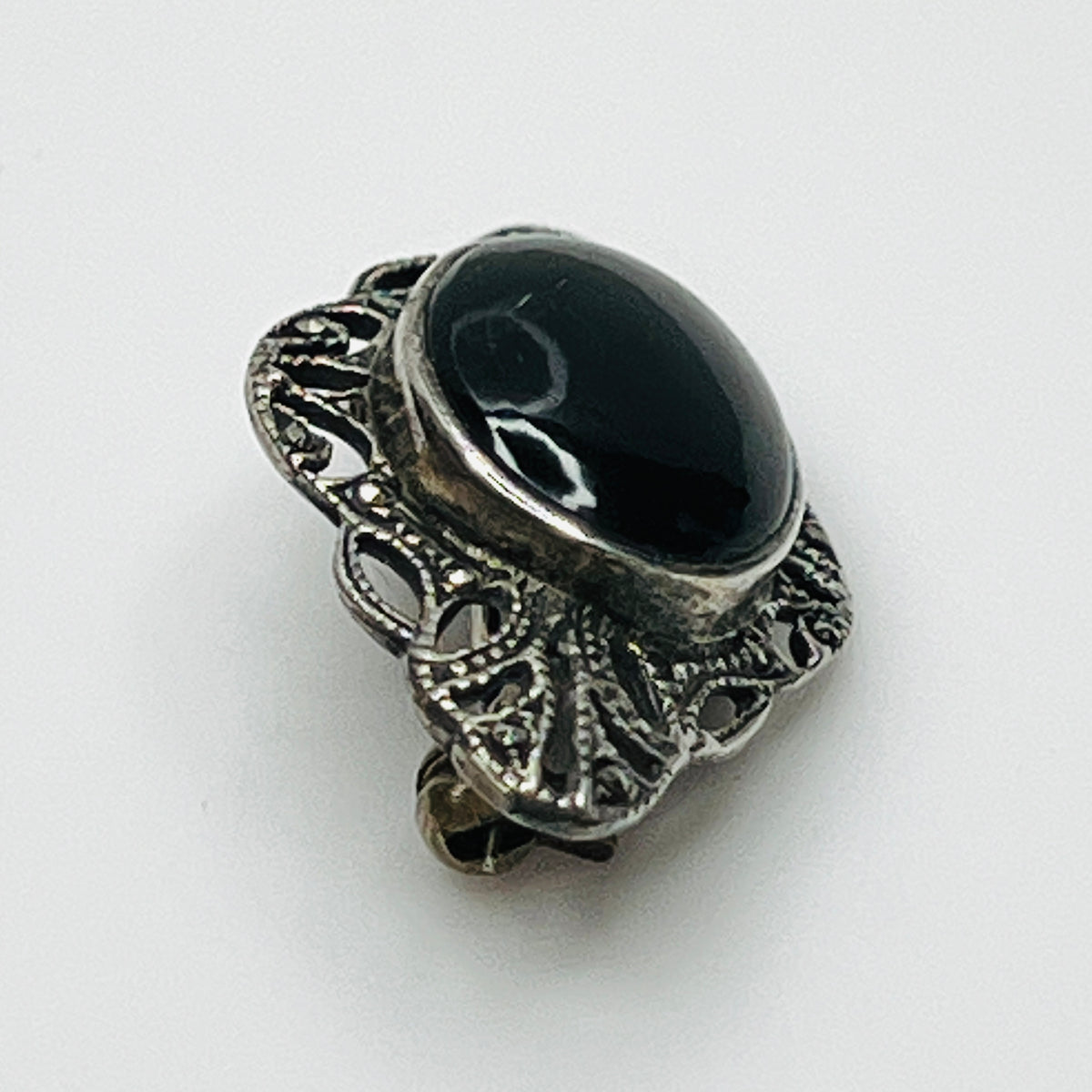 Angled view of vintage black onyx cabochon brooch showing raised bezel and intricate marcasite filigree.