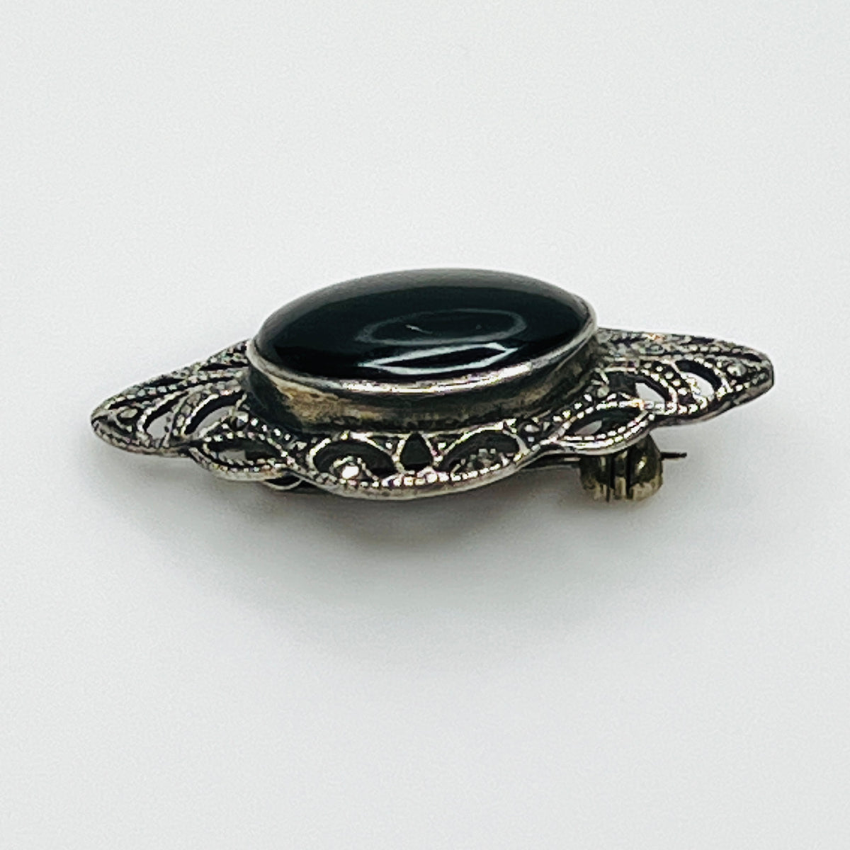 Angled view of vintage black onyx cabochon brooch showing raised bezel and intricate marcasite filigree.
