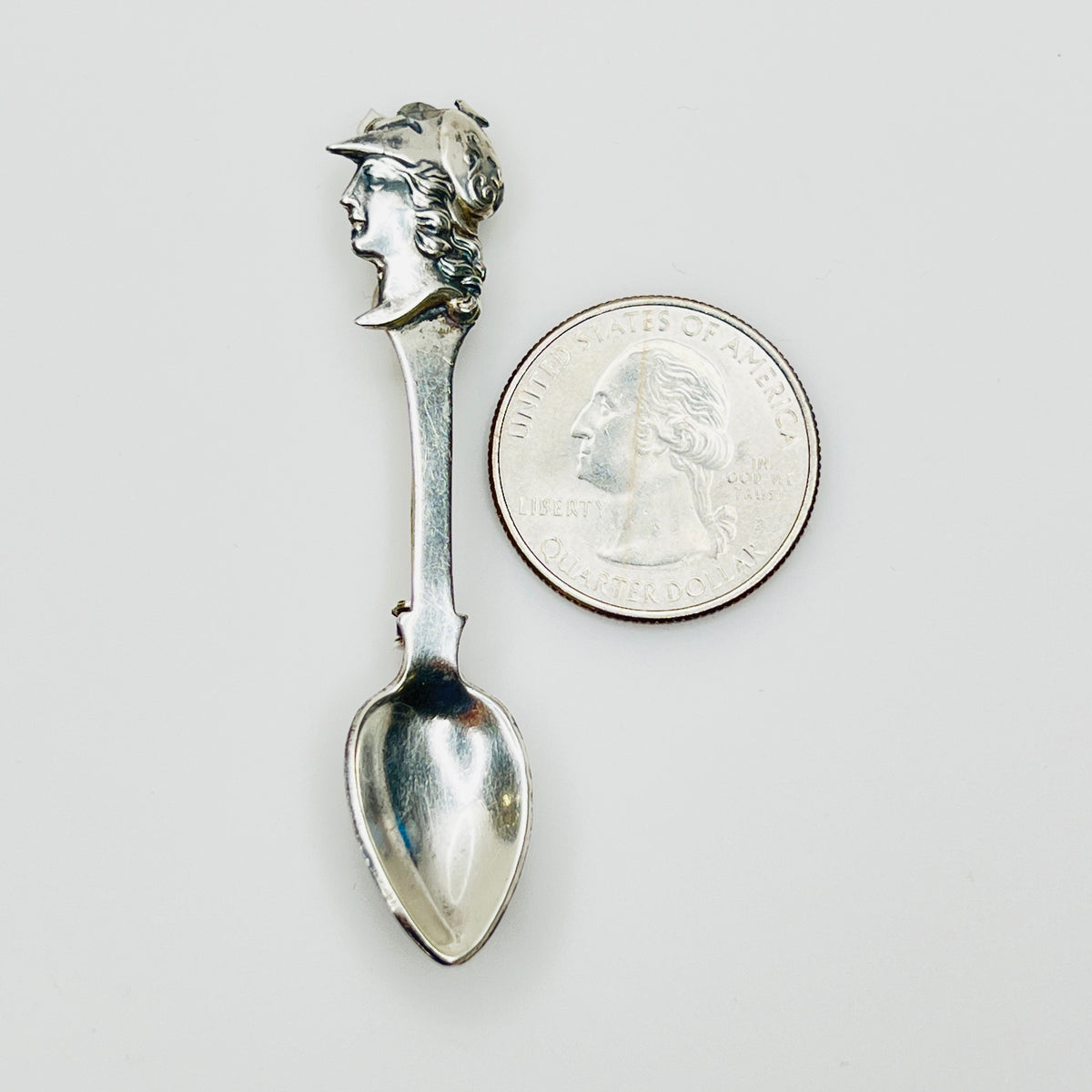 Sterling silver figural spoon pin next to coin for scale