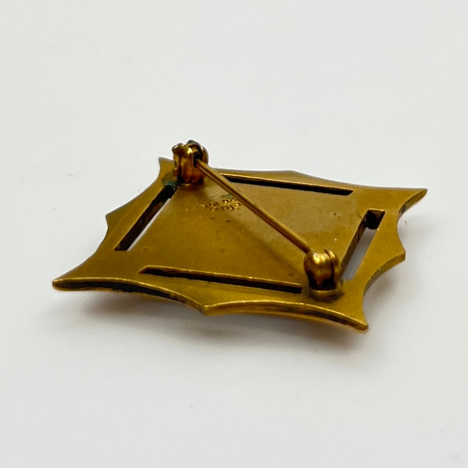 Angled view of cTo enamel brooch with raised medallion and deco-style edges