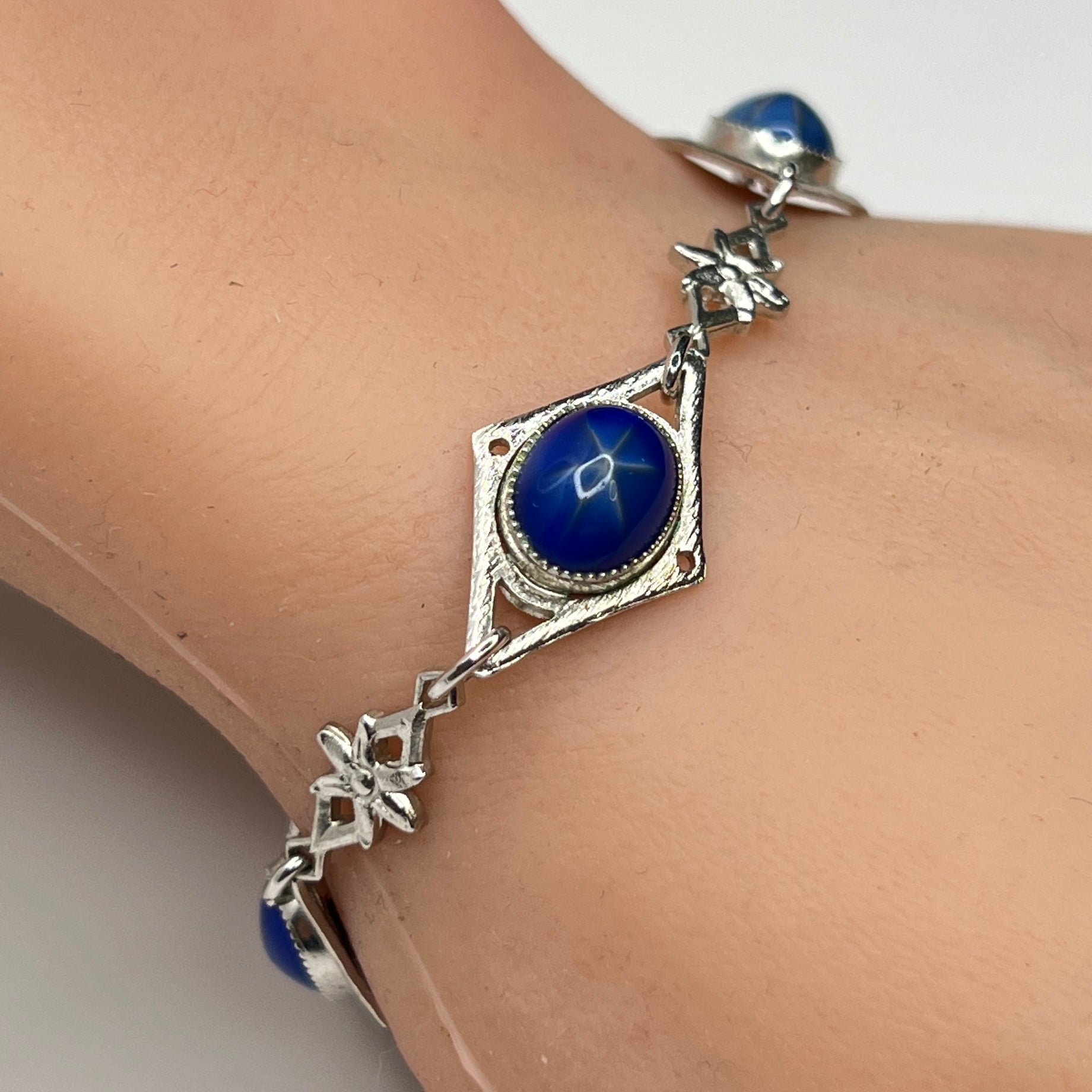 Faux star sapphire bracelet on wrist with silver-tone floral links
