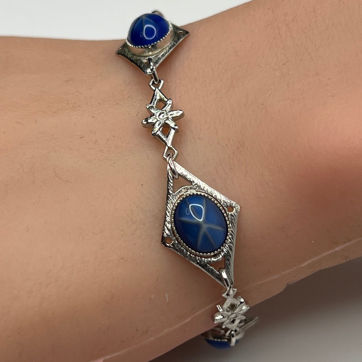 Faux star sapphire bracelet on wrist with silver-tone floral links