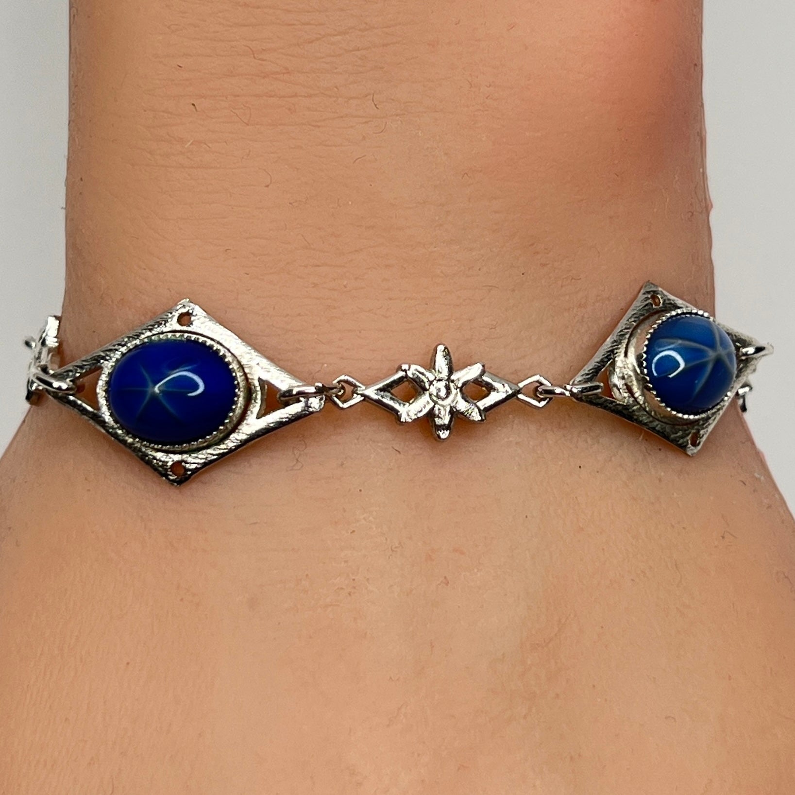 Faux star sapphire bracelet on wrist with silver-tone floral links