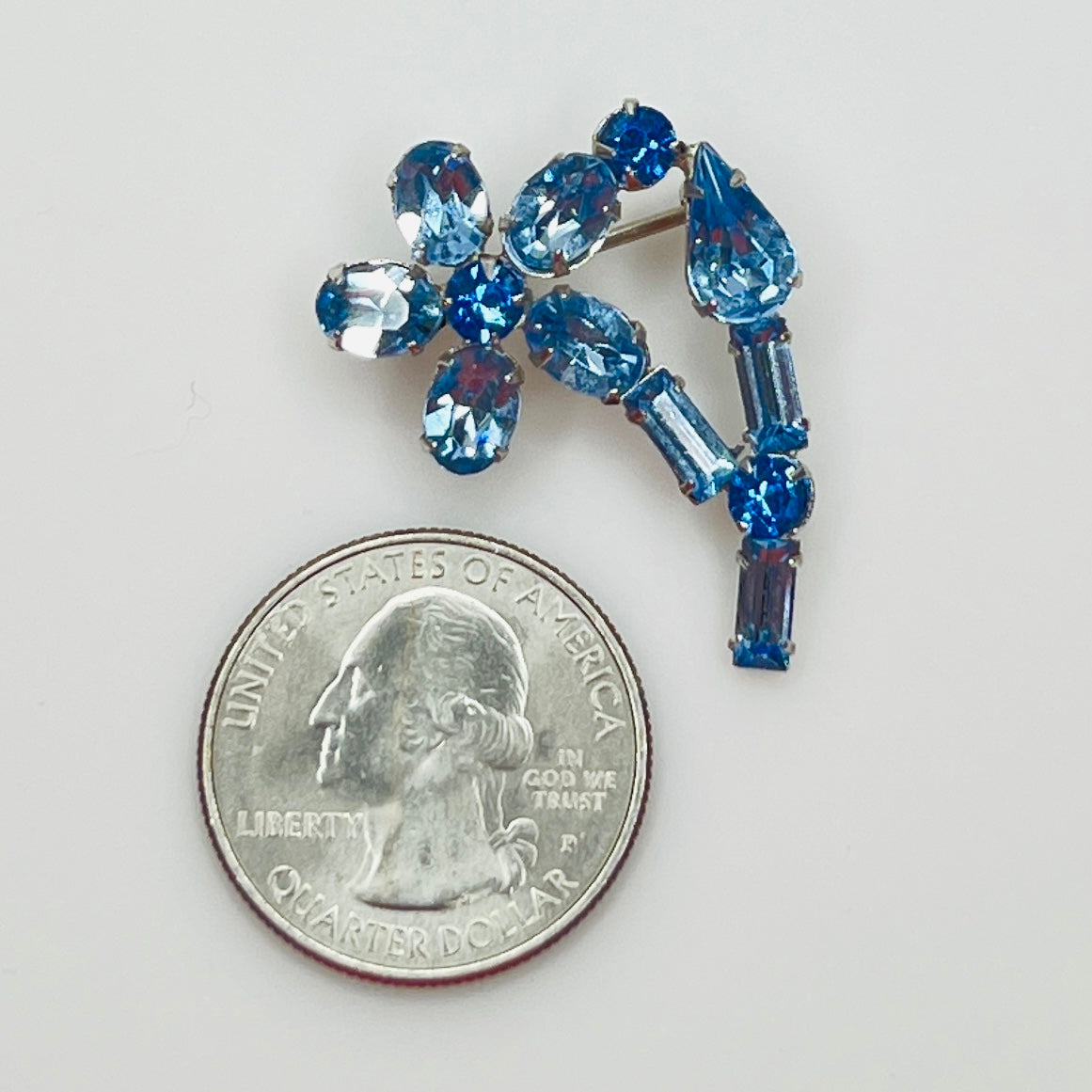 Small sapphire rhinestone brooch shown next to U.S. quarter for scale