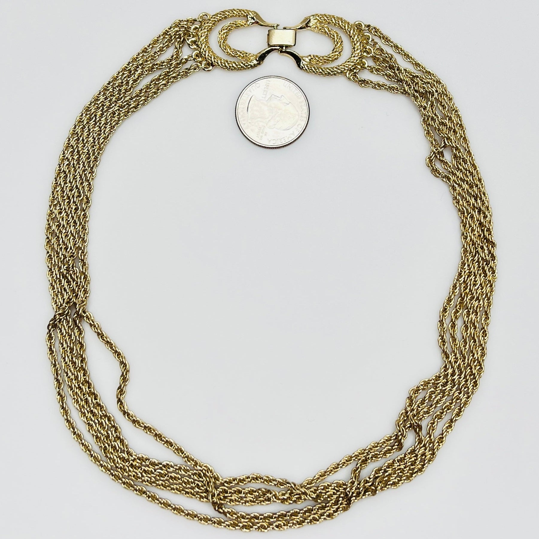 multi-strand gold tone chain necklace shown on flat surface with quarter for scale