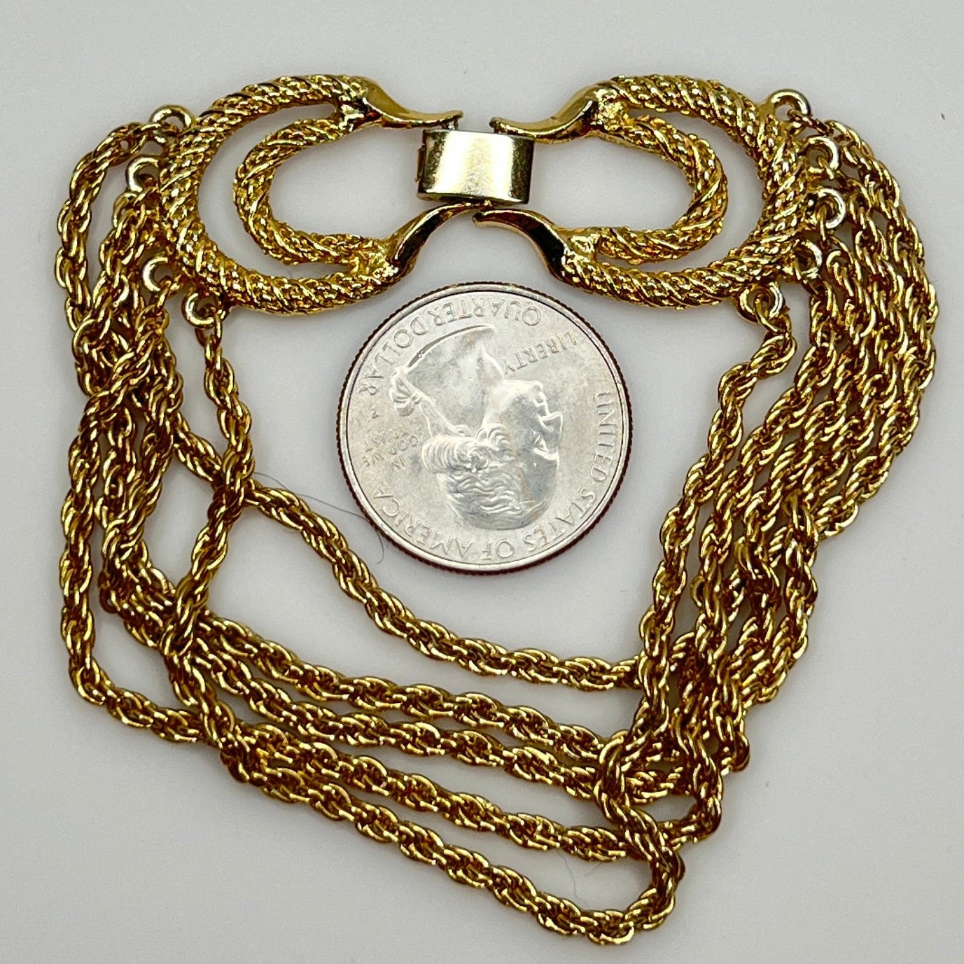 multi-strand gold tone chain bracelet shown on flat surface with quarter for scale