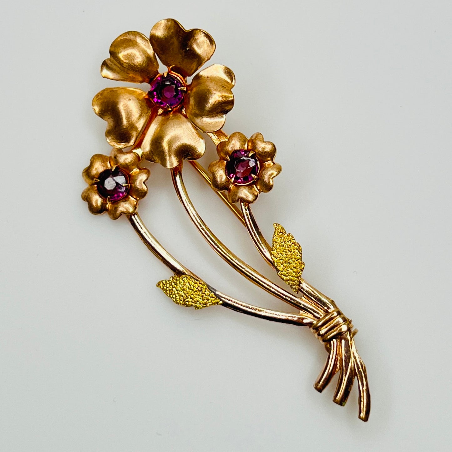 1950s gold-tone brooch with three purple rhinestone flowers and textured gold leaves