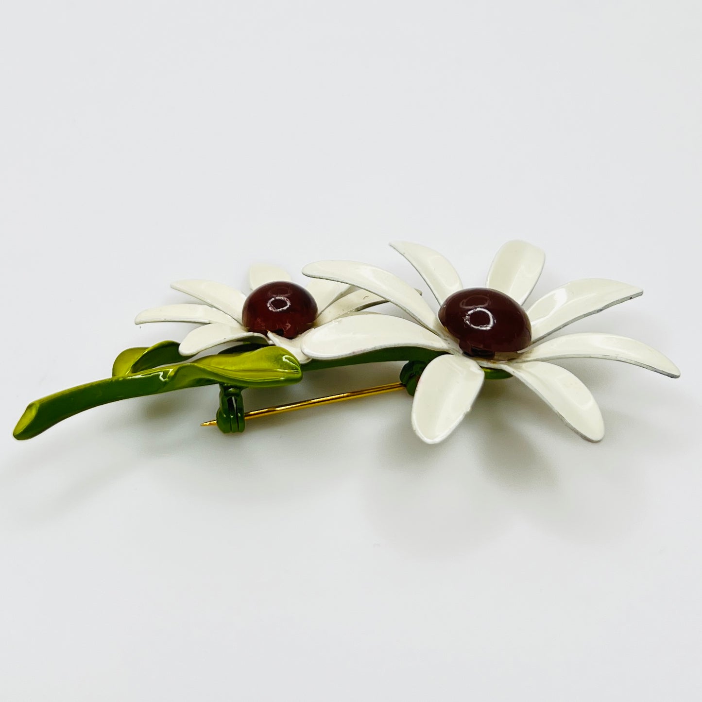 Floral brooch with white flowers and green leaves on a light gray background