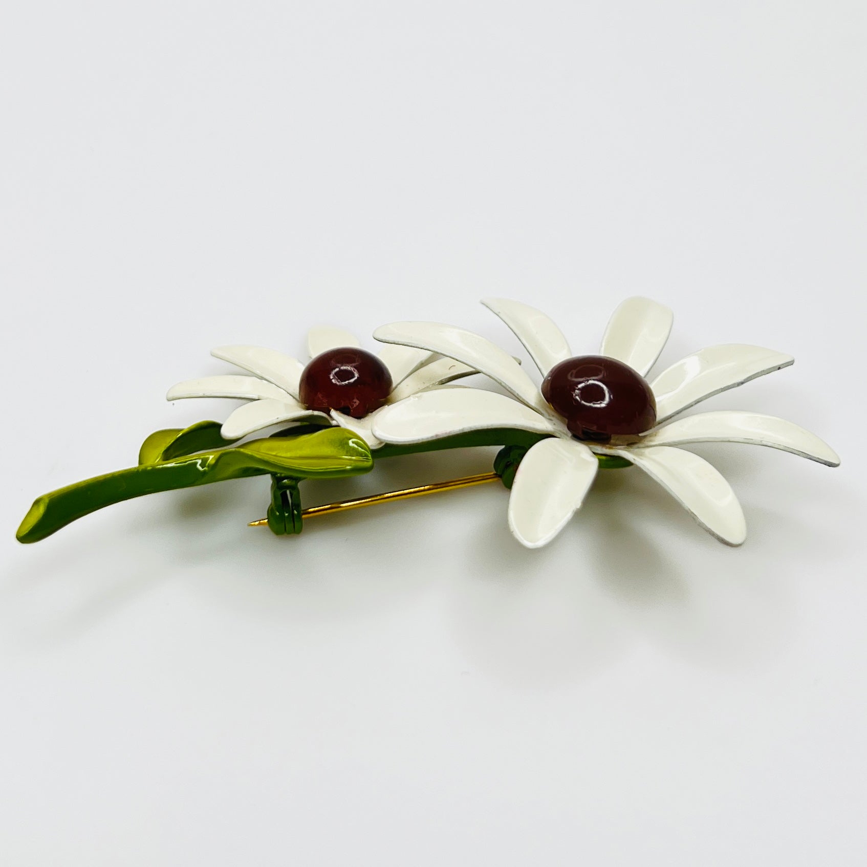 Floral brooch with white flowers and green leaves on a light gray background