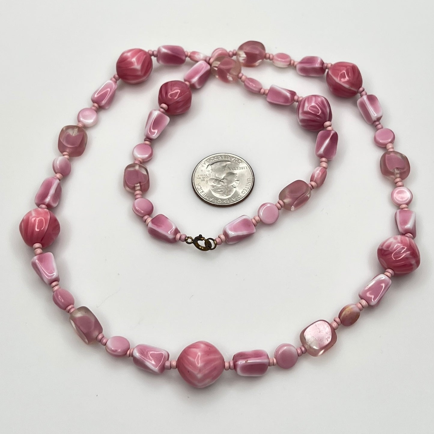 Close-up of mixed pink glass beads in various shapes and finishes with brass clasp