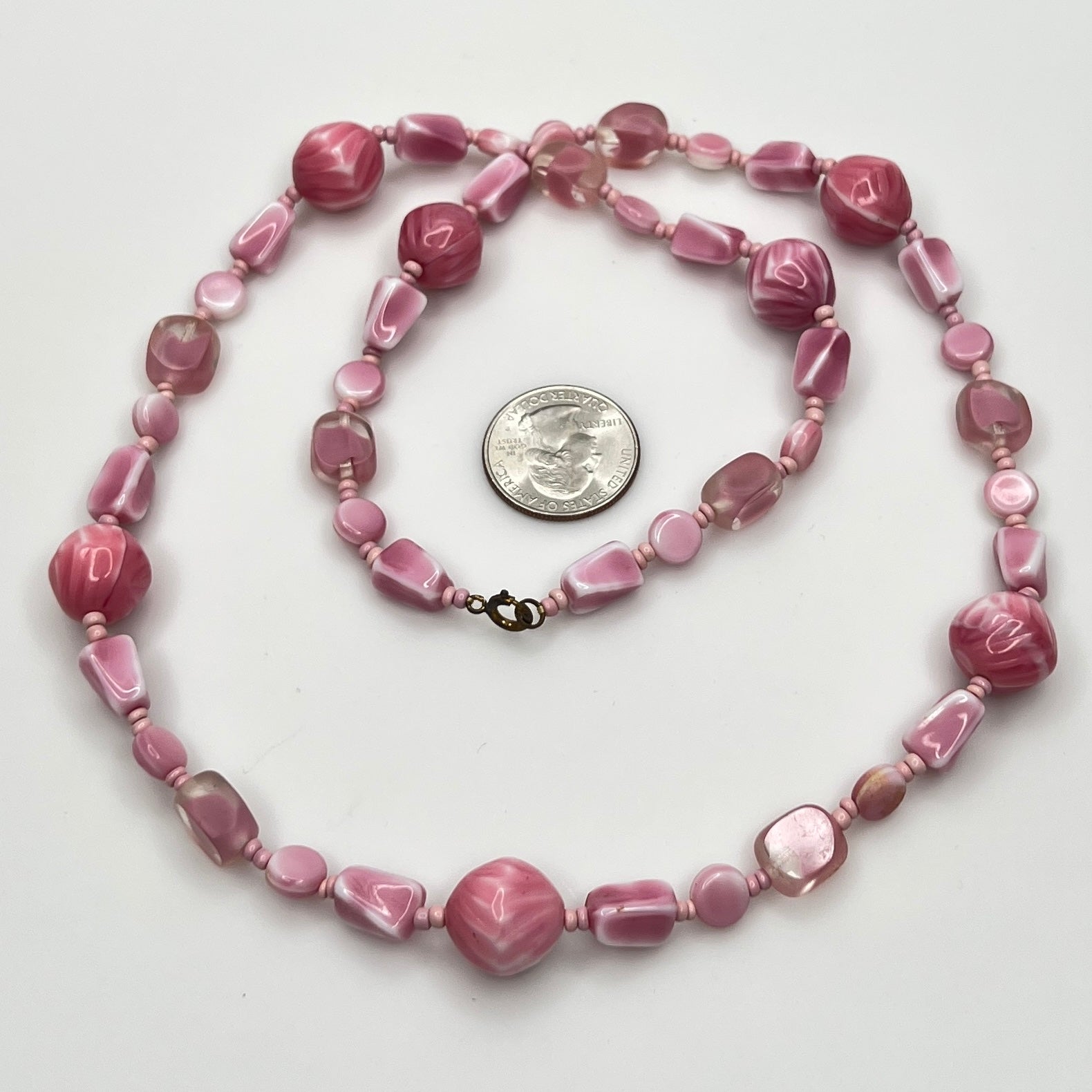 Close-up of mixed pink glass beads in various shapes and finishes with brass clasp