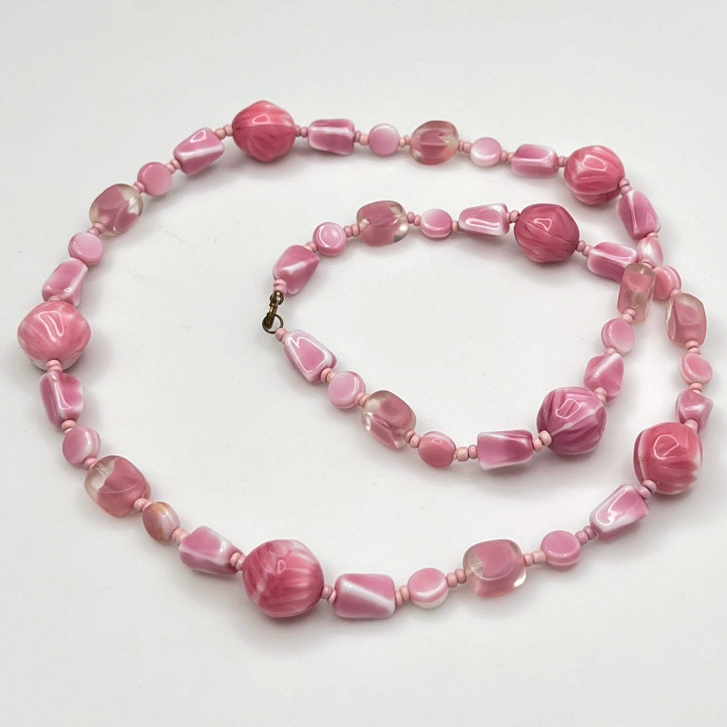Close-up of mixed pink glass beads in various shapes and finishes with brass clasp