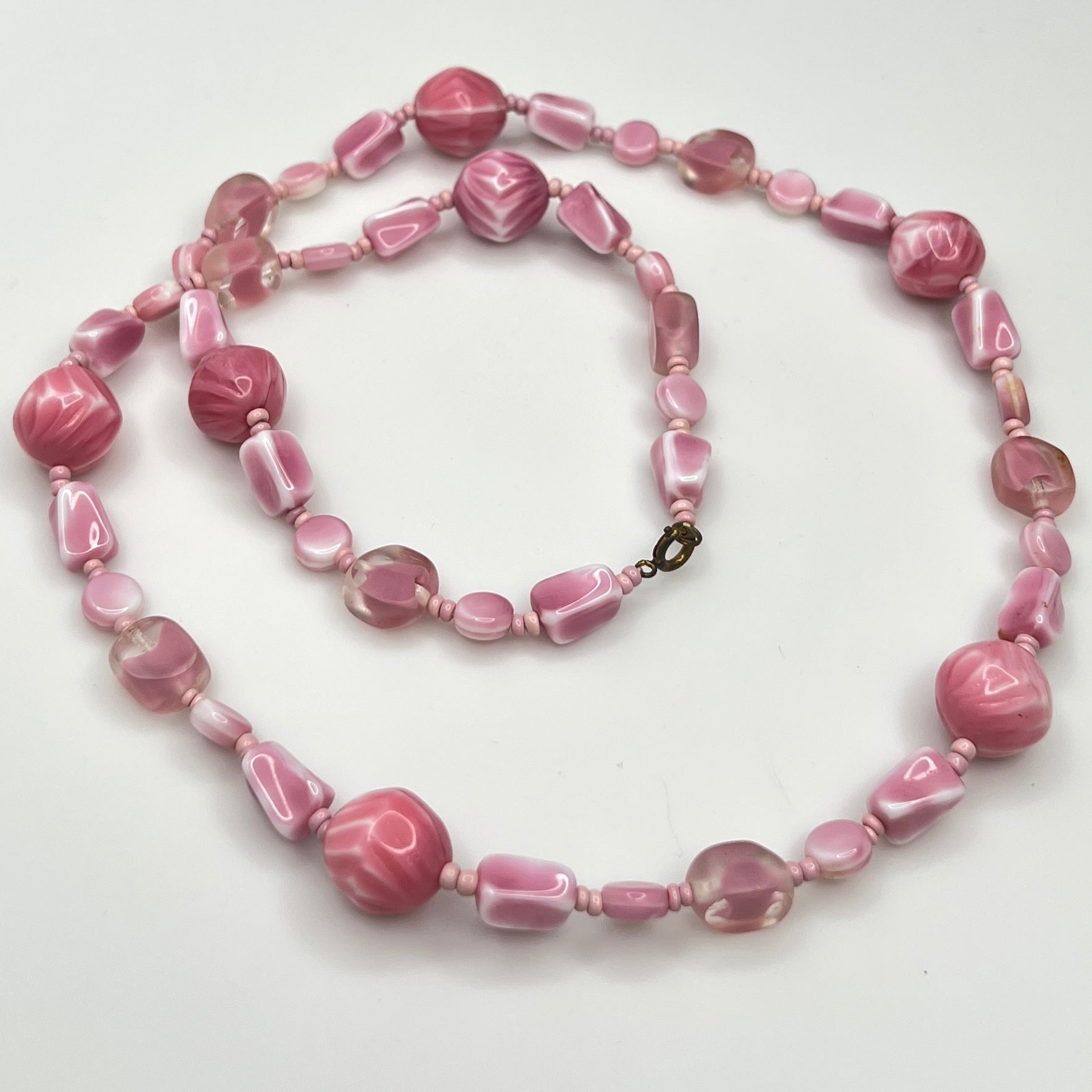 Close-up of mixed pink glass beads in various shapes and finishes with brass clasp