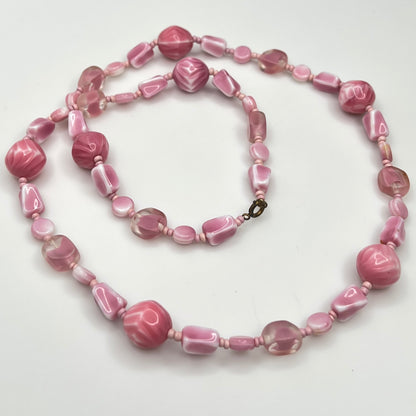 Close-up of mixed pink glass beads in various shapes and finishes with brass clasp