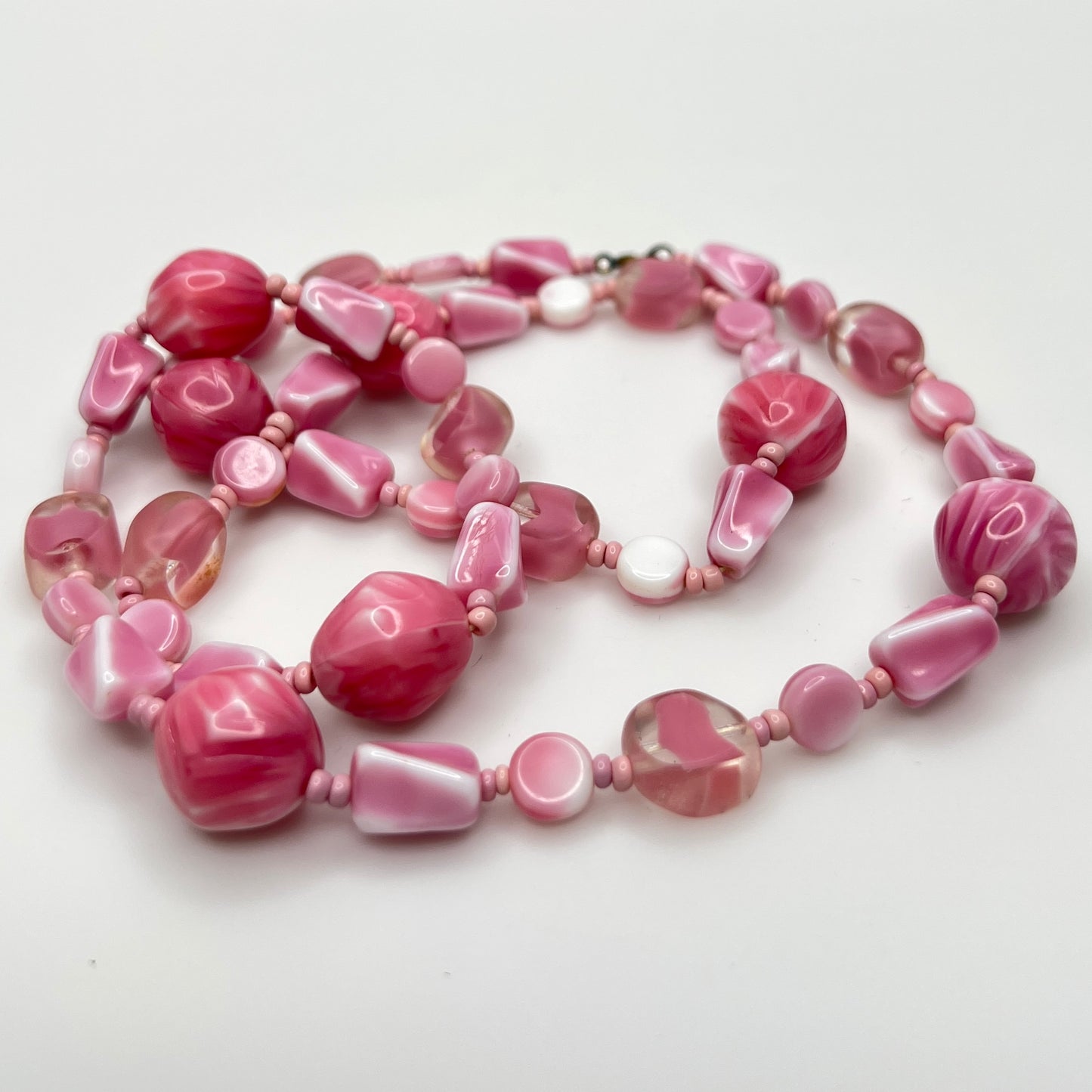Close-up of mixed pink glass beads in various shapes and finishes with brass clasp