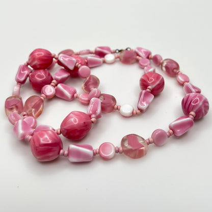Close-up of mixed pink glass beads in various shapes and finishes with brass clasp