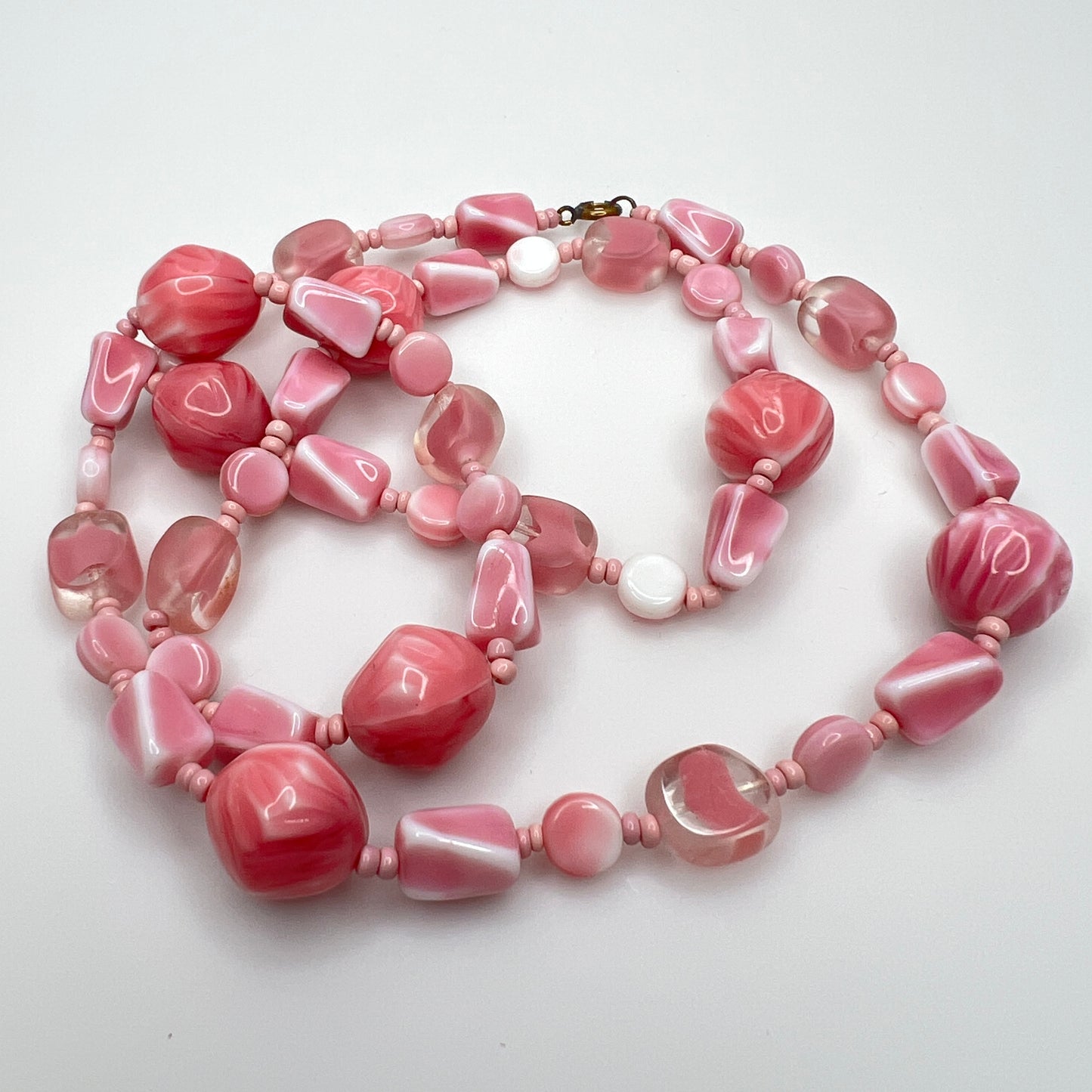 Close-up of mixed pink glass beads in various shapes and finishes with brass clasp