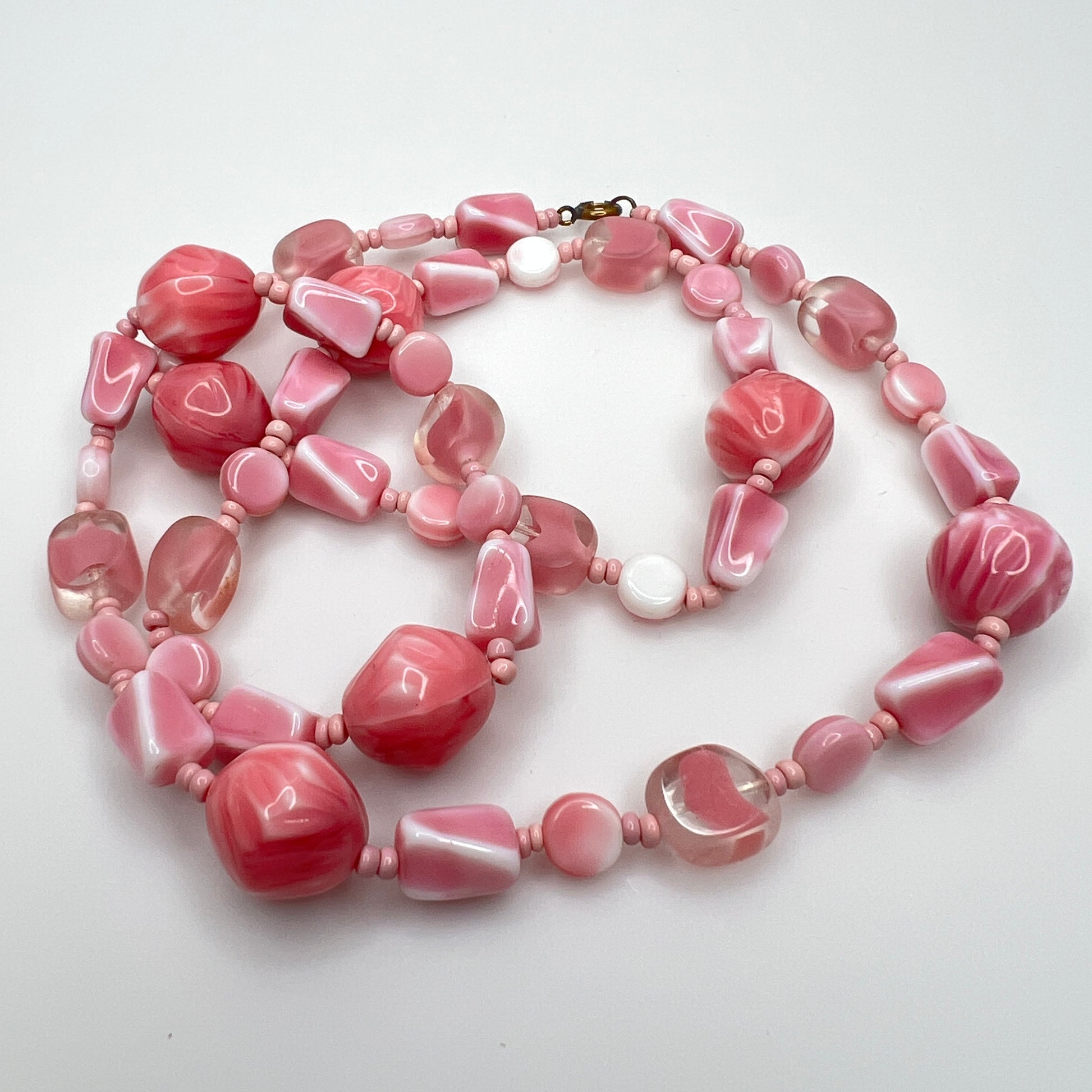 Close-up of mixed pink glass beads in various shapes and finishes with brass clasp