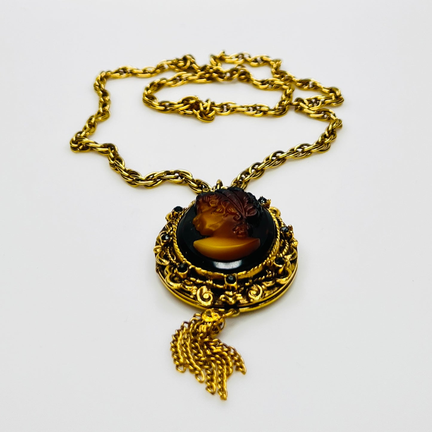 Side view of cameo locket with decorative scrollwork and tassel
