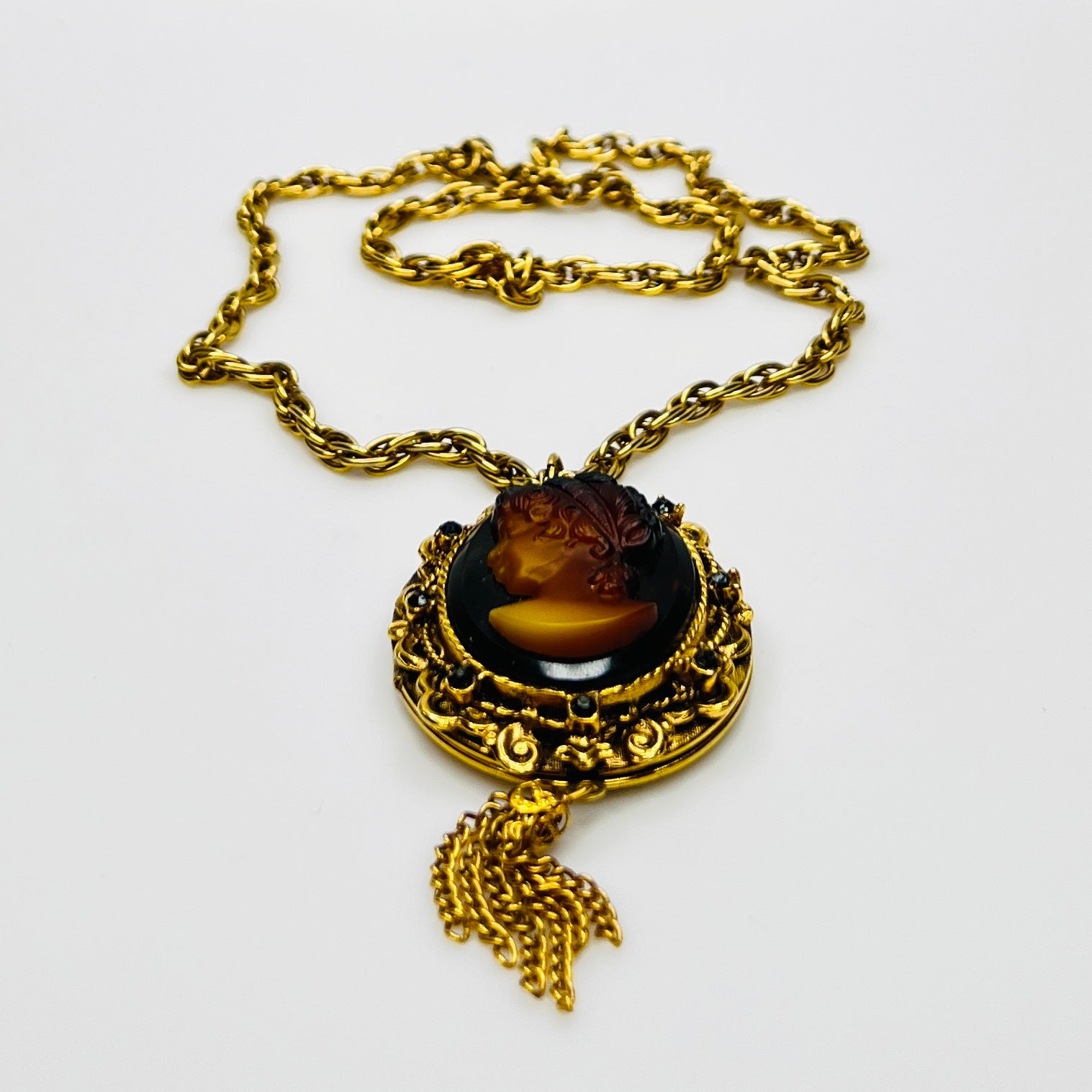 Side view of cameo locket with decorative scrollwork and tassel