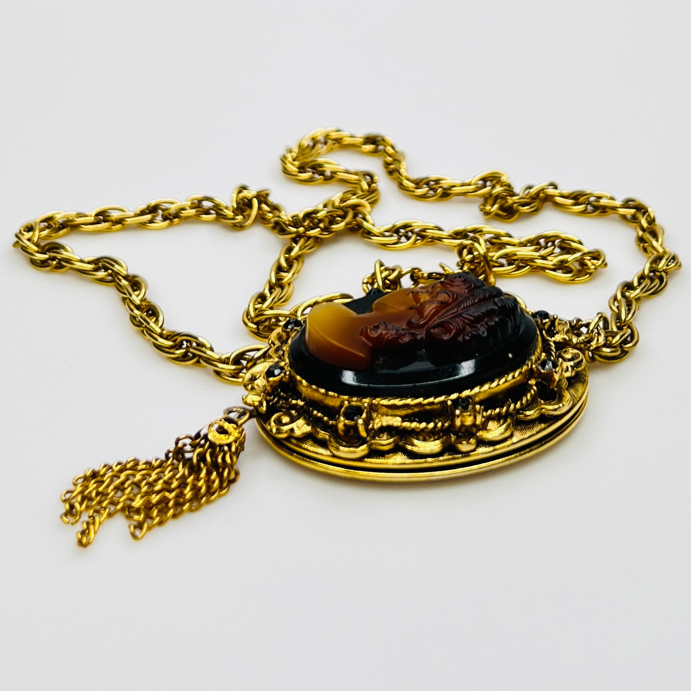 Side view of cameo locket with decorative scrollwork and tassel