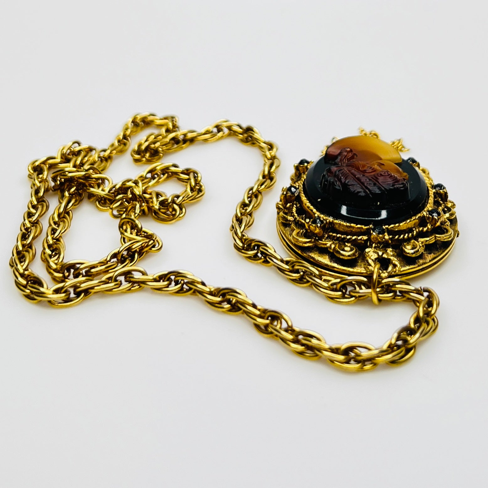 Side view of cameo locket with decorative scrollwork and tassel