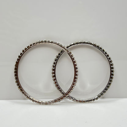 Set of two silver-tone bangle bracelets with prong-set clear rhinestones, vintage 1980s.