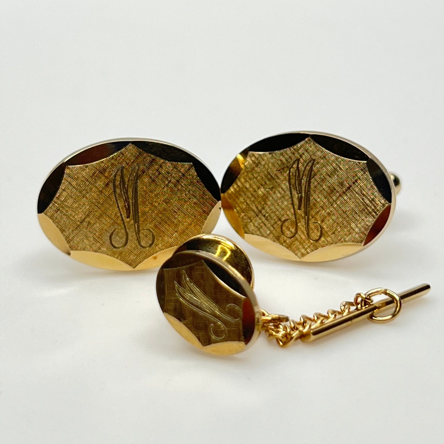 Close-up of monogrammed “M” cufflinks and matching gold-tone tie tack