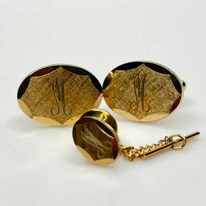Close-up of monogrammed “M” cufflinks and matching gold-tone tie tack