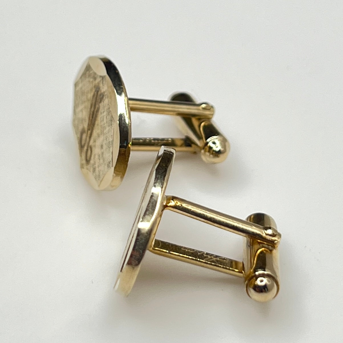 Close-up of monogrammed “M” cufflinks and matching gold-tone tie tack