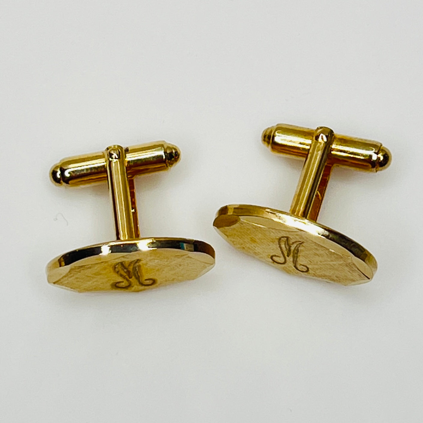 Close-up of monogrammed “M” cufflinks and matching gold-tone tie tack