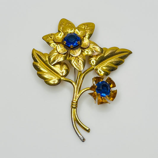 Vintage brass flower brooch with two sapphire-blue rhinestones and leaf details, 1940s style.