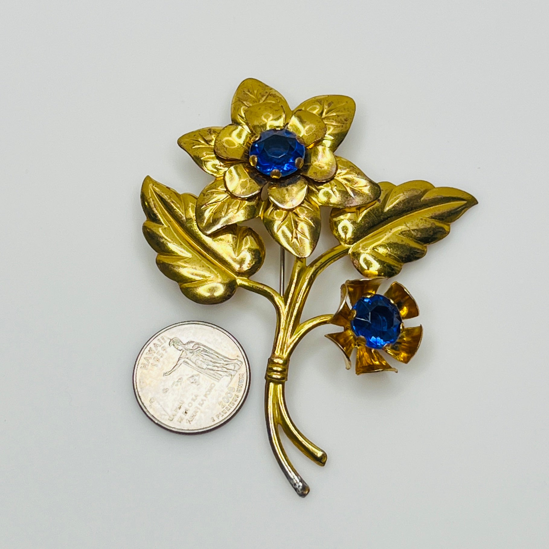 Vintage brass flower brooch with two sapphire-blue rhinestones and leaf details, 1940s style.