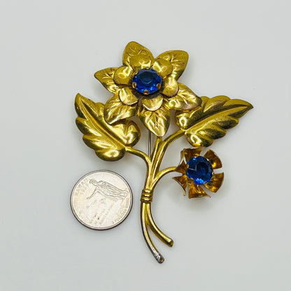 Vintage brass flower brooch with two sapphire-blue rhinestones and leaf details, 1940s style.