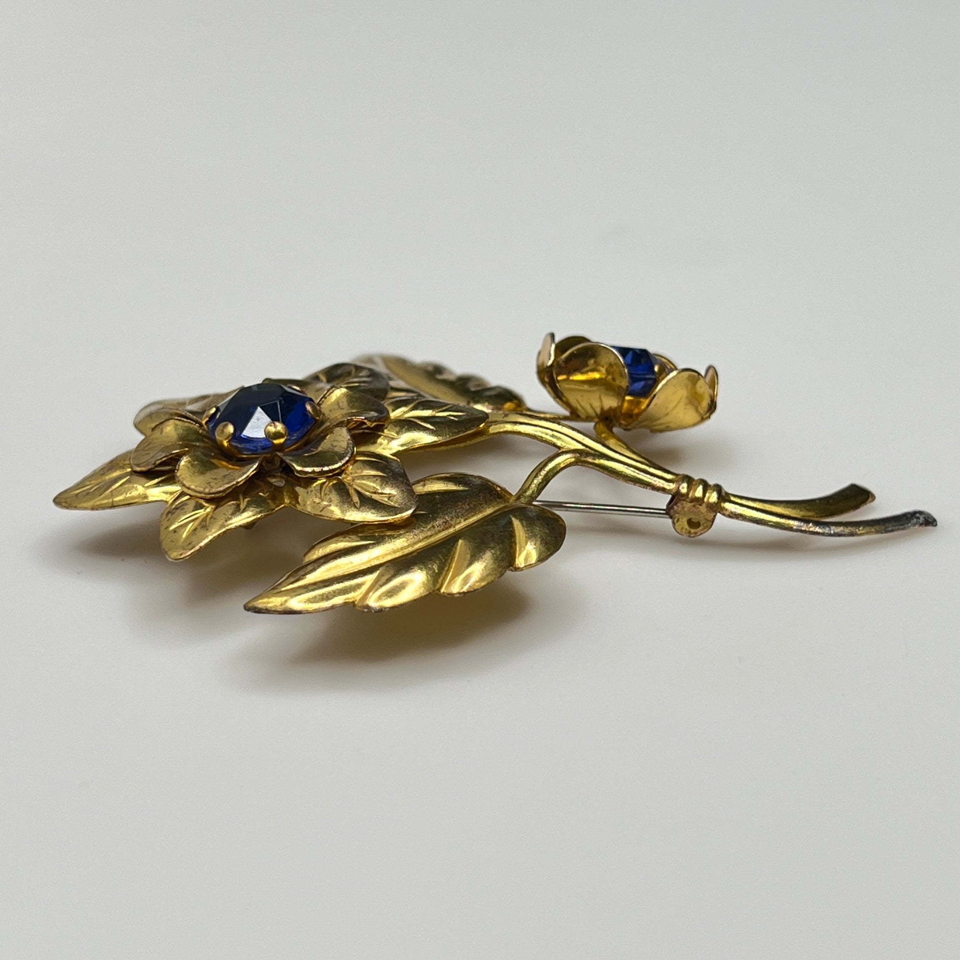 Gold floral brooch with blue gemstones on a light gray background
