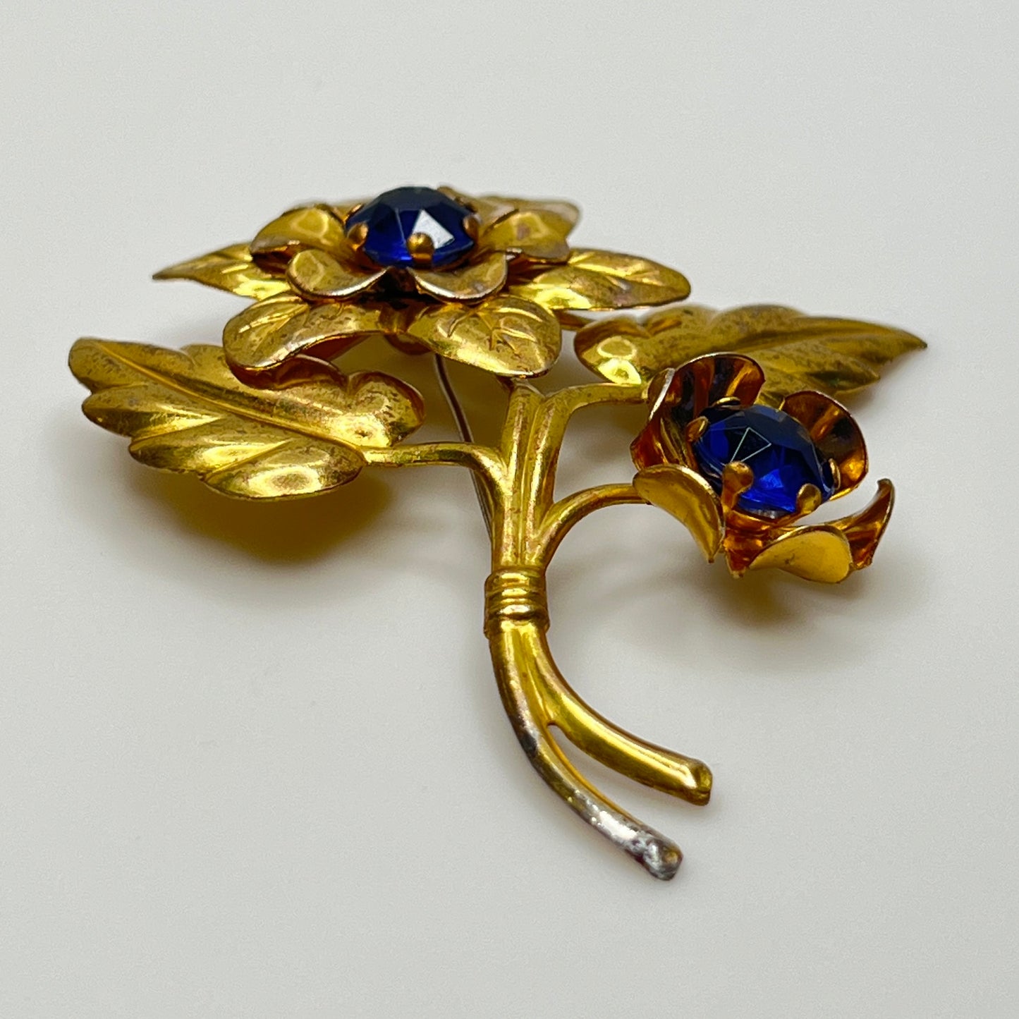 Vintage brass flower brooch with two sapphire-blue rhinestones and leaf details, 1940s style.
