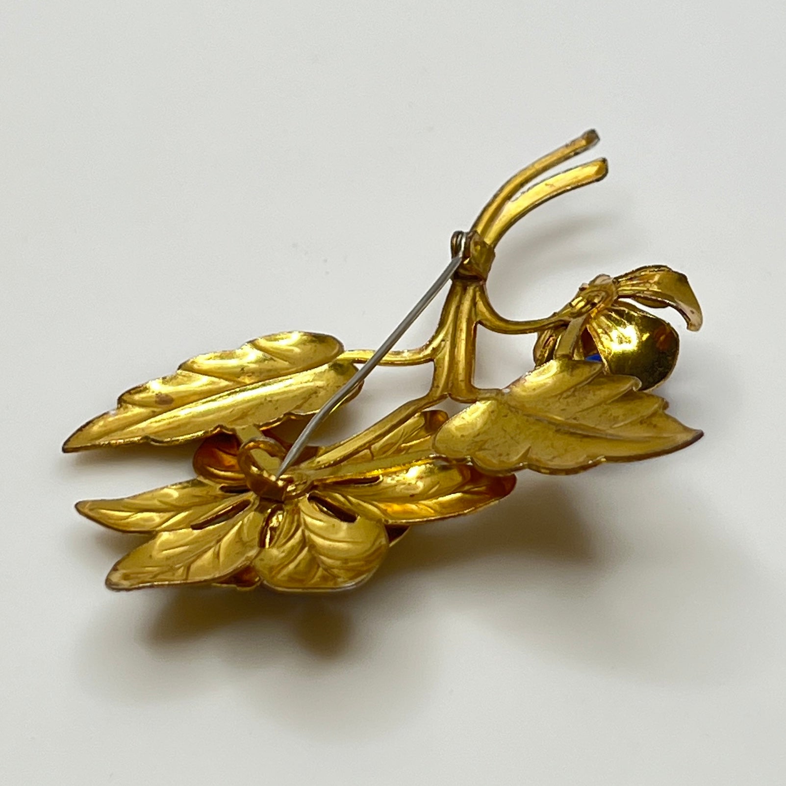 Vintage brass flower brooch with two sapphire-blue rhinestones and leaf details, 1940s style.