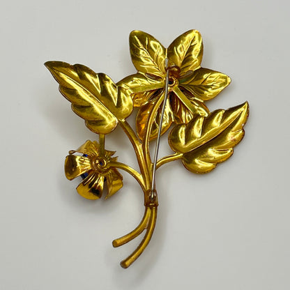Vintage brass flower brooch with two sapphire-blue rhinestones and leaf details, 1940s style.