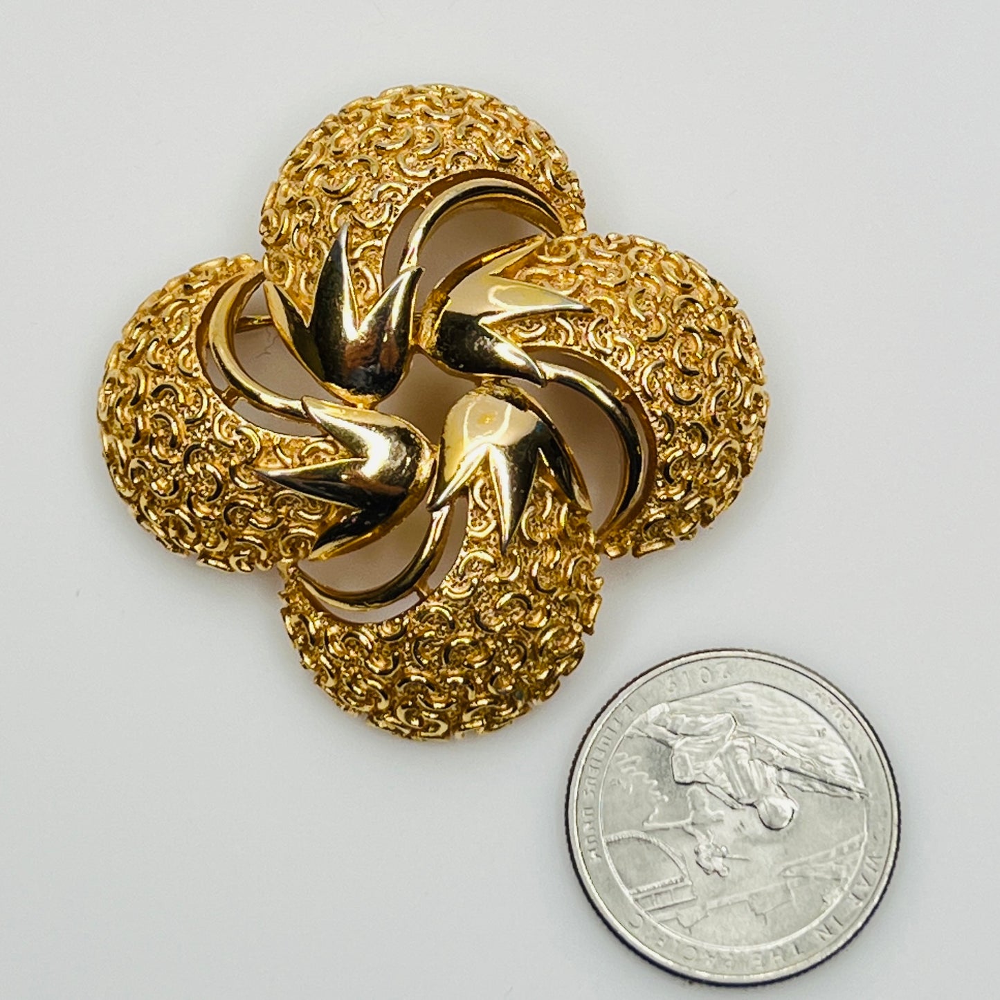 Crown Trifari gold swirl brooch with clover-style textured domes with US quarter for size comparison