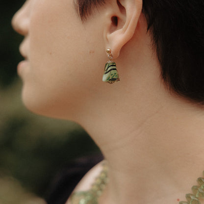 Close-up of a person wearing a green and gold earring with a blurred background