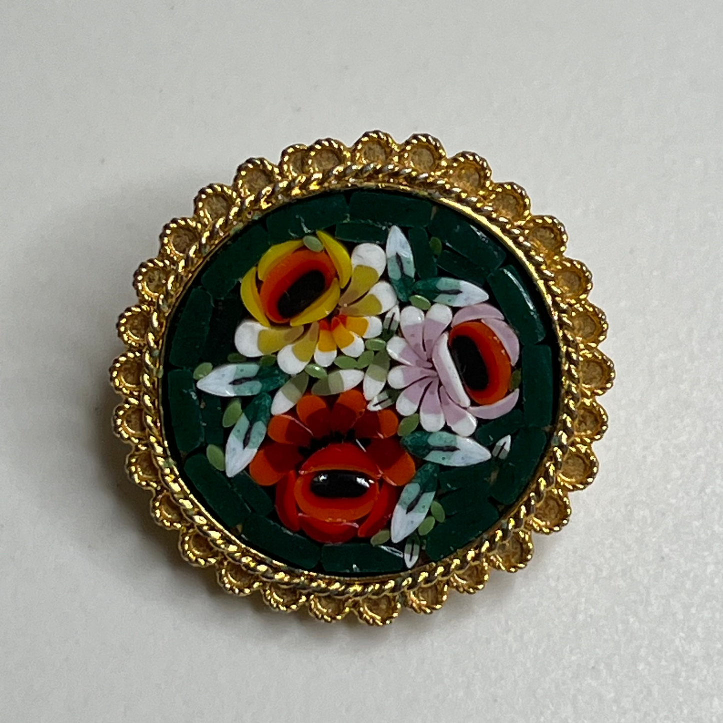 Close-up of round micro mosaic pin with red, pink, and yellow flowers