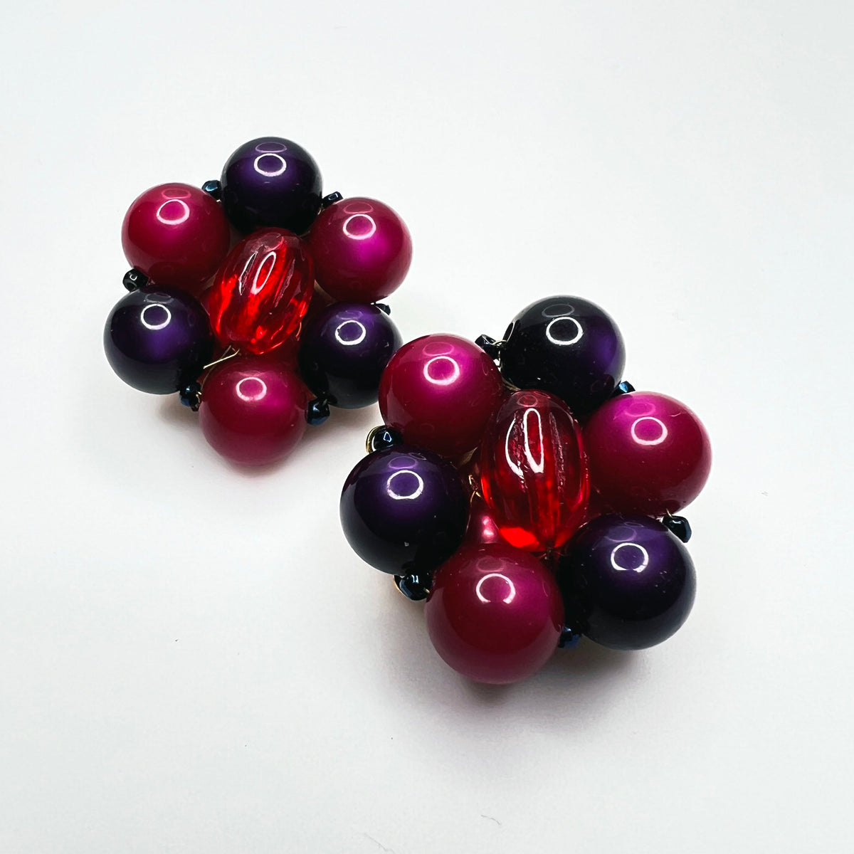 Marvella clip earrings featuring purple and pink moonglow beads surrounding translucent red oval beads.