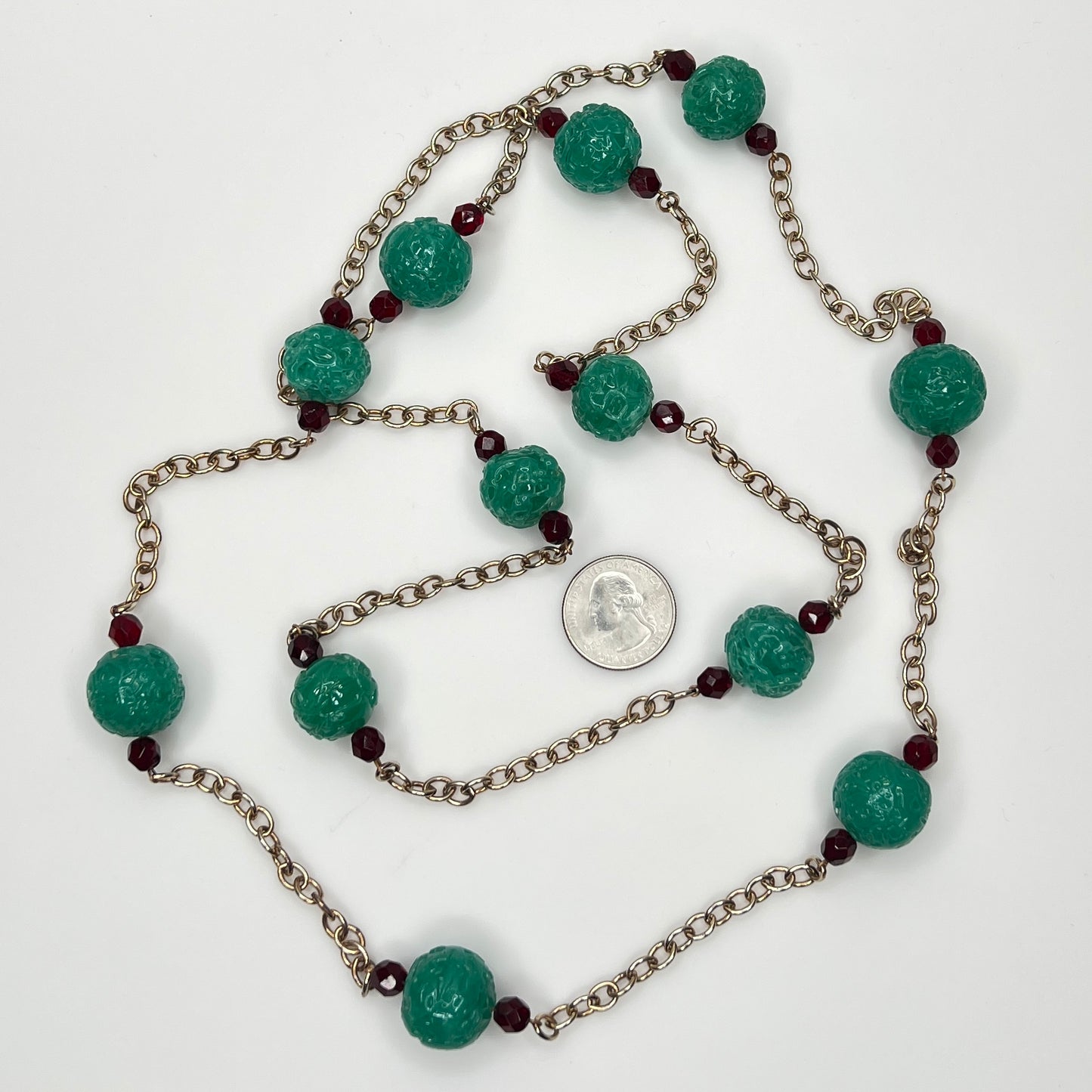 Close-up of textured green art glass beads with red faceted accents and gold chain with a US quarter for size.