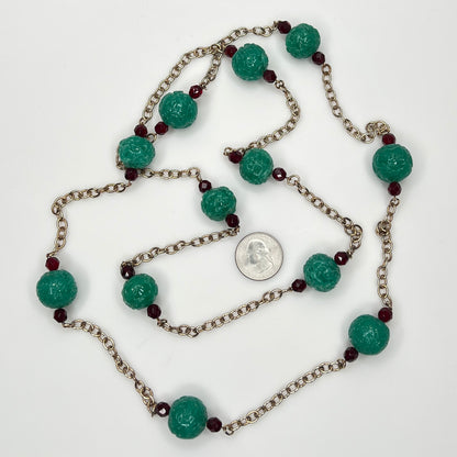 Close-up of textured green art glass beads with red faceted accents and gold chain with a US quarter for size.