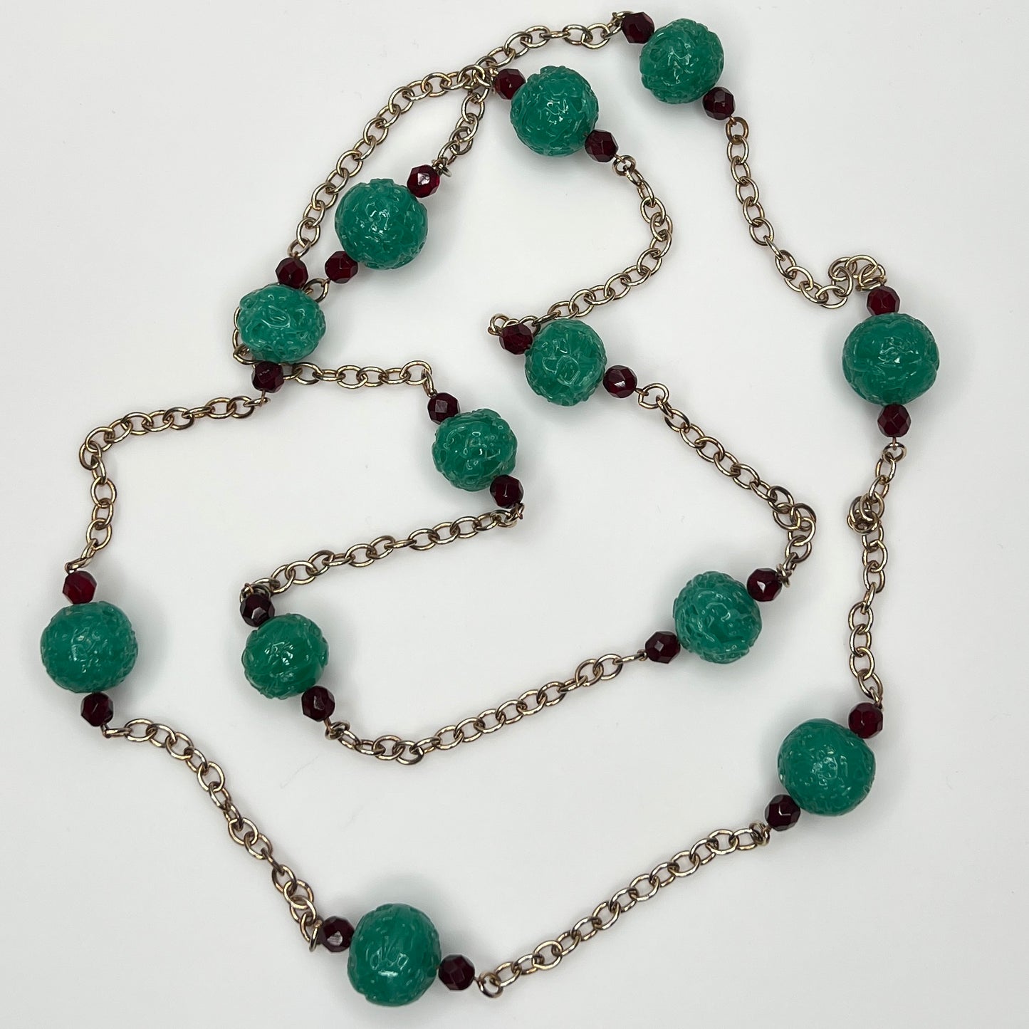 Close-up of textured green art glass beads with red faceted accents and gold chain