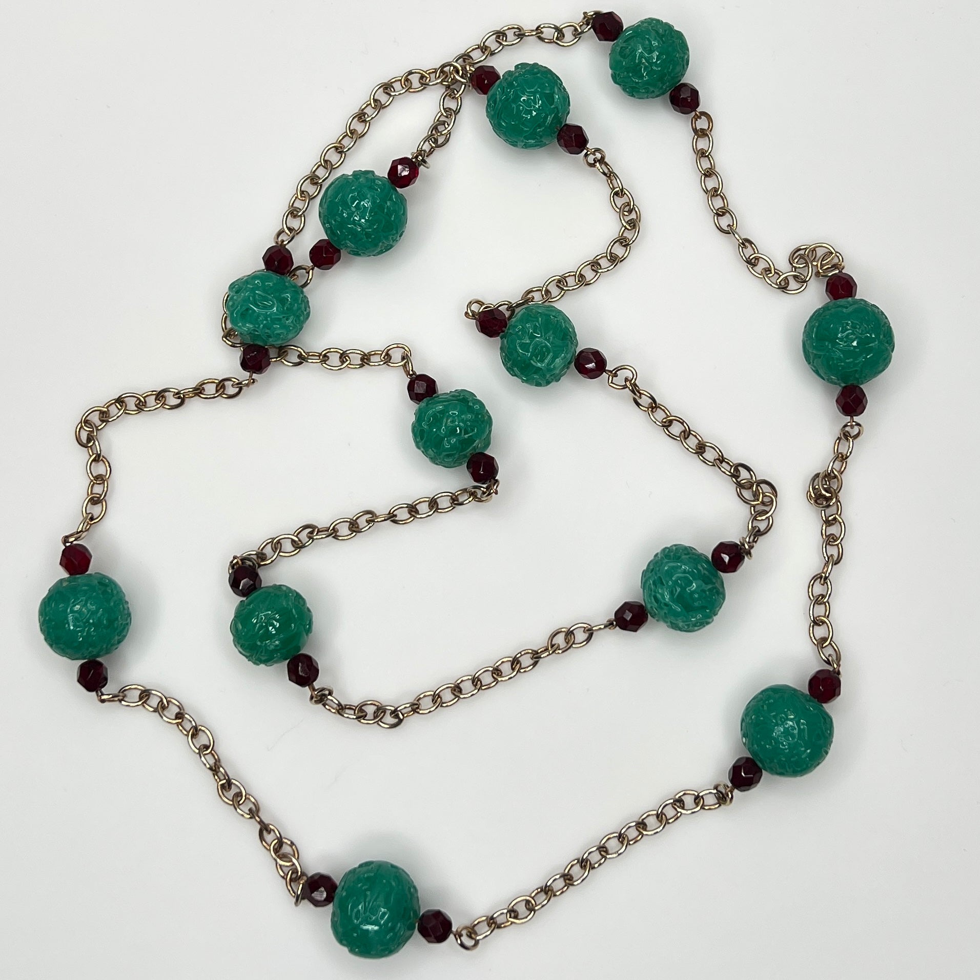 Close-up of textured green art glass beads with red faceted accents and gold chain
