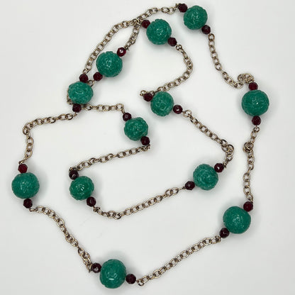 Close-up of textured green art glass beads with red faceted accents and gold chain