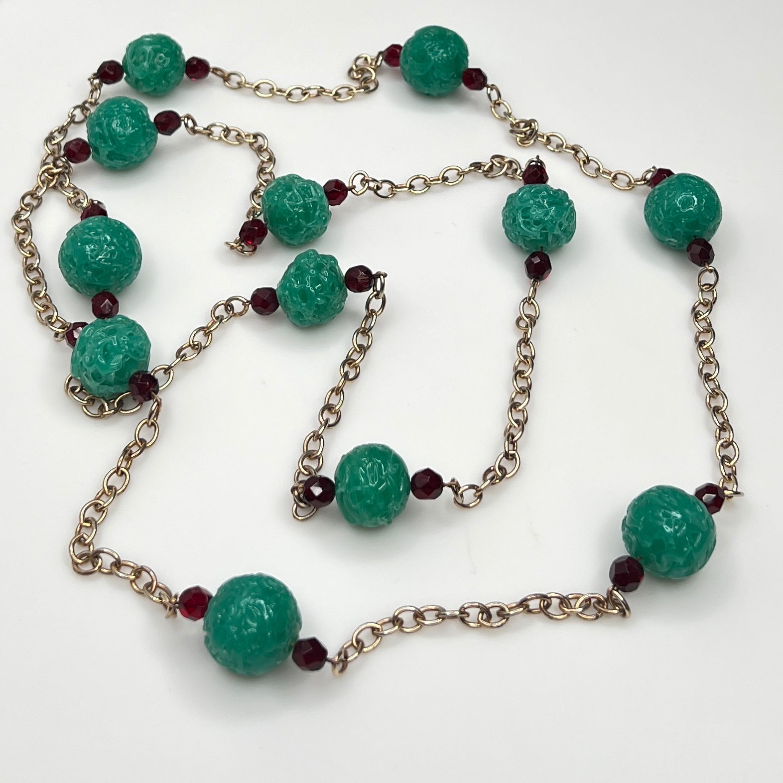 Close-up of textured green art glass beads with red faceted accents and gold chain