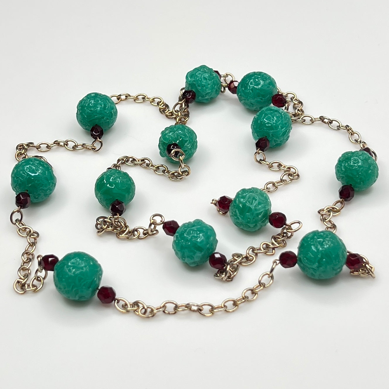 Close-up of textured green art glass beads with red faceted accents and gold chain